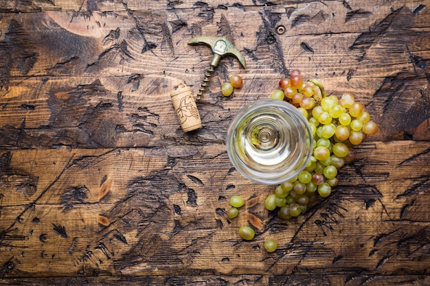 Glas witte wijn en rijpe druiven op houten ondergrond, bovenaanzicht