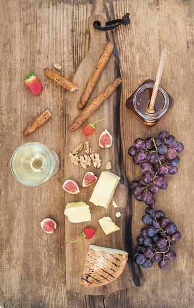 Glas witte wijn, kaasplank, druiven, vijgen, aardbeien, honing en broodstengels