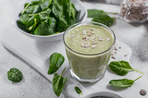 Glas zelfgemaakte gezonde groene smoothie met verse baby spinazie zonnebloemen en sesamzaadjes op lichte achtergrond eten en drinken dieet en gezond eten concept