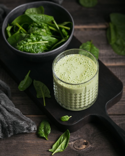 Glas zelfgemaakte gezonde groene smoothie met verse babyspinazie op donkere achtergrond. eten en drinken, diëten en gezond eten concept