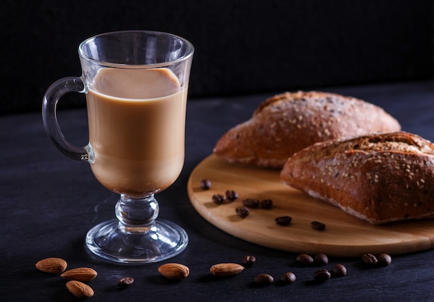 Glaskop koffie met room en broodjes op een zwarte achtergrond