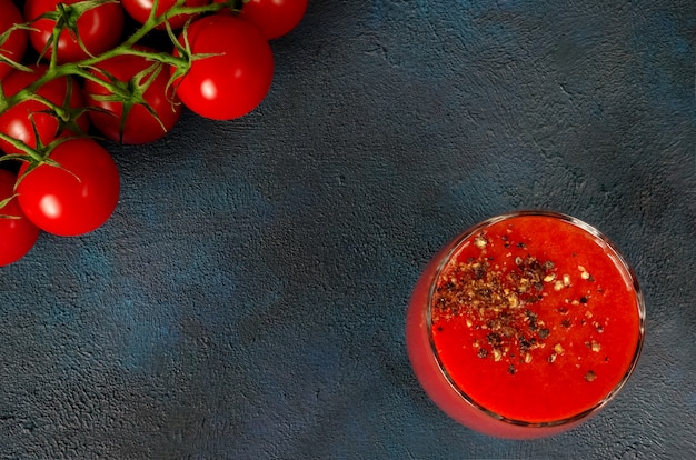 Glaskop met tomatensap met gemalen zwarte peper en kerstomaatjes op donker