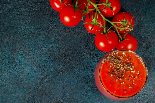 Glaskop met tomatesap met gemalen zwarte peper en kersentomaten op donkere achtergrond