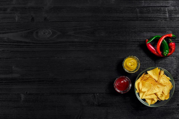 Glasplaat met maïschips nacho's en tomatensaus op een zwarte houten tafelbladplaats voor tekst