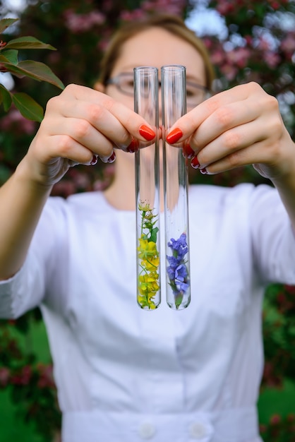 Glasreageerbuizen met bloemsteekproeven, close-up. Vrouwelijke handen die vage flessen houden. Studie van planten, geneeskrachtige kruiden, creatie van natuurlijke bloemenaroma's. Reclame parfumindustrie.