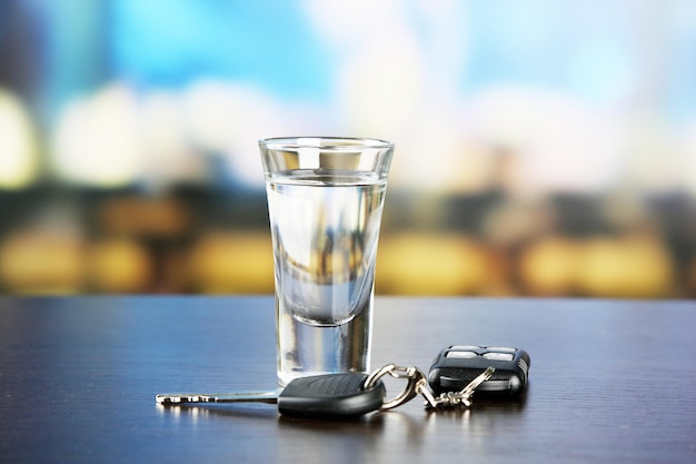 Glass of alcoholic drink and car key on wooden table on light background