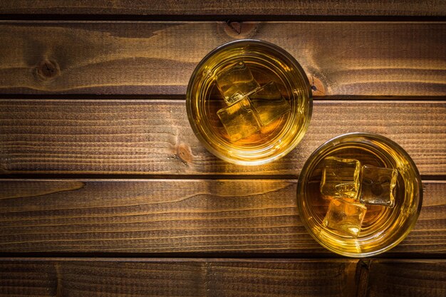 Photo glass of alcoholic drink with ice cubes on wooden table