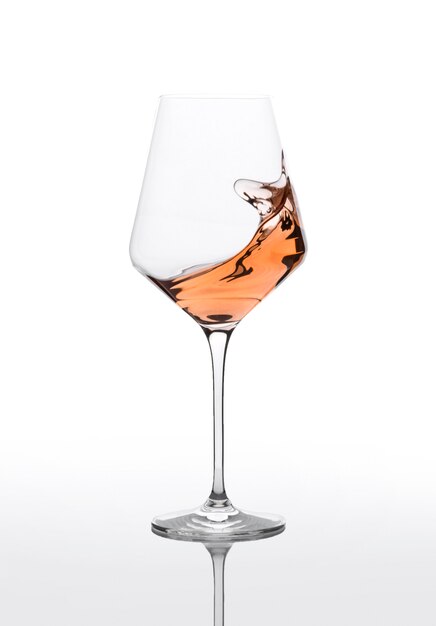 Glass of amber wine with splashes on white table.