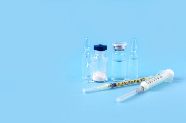 Стеклянные ампулы с вакциной и шприцы на синем фоне. Прививка против Ковид 19