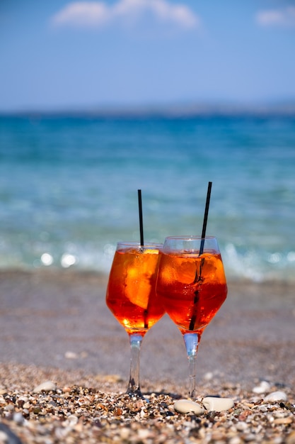 Glass of aperol spritz cocktail stands on sand near the sea