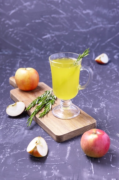 A glass of apple cider with rosemary and apples