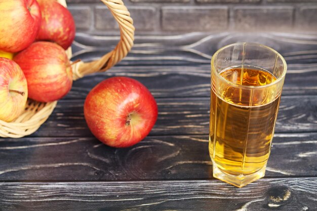 A glass of apple juice and red apples on a dark wooden surface