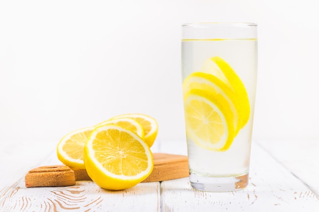 Стеклянный стакан и кувшин холодного лимонада на белом фоне деревянные, в окружении лимонов.