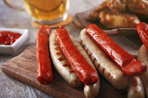 Glass of beer chicken wings and grilled sausages on wooden table close up