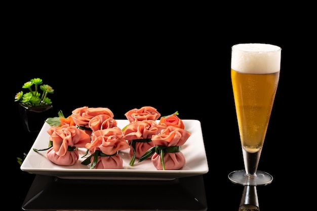 a glass of beer next to a plate of mortadella appetizer