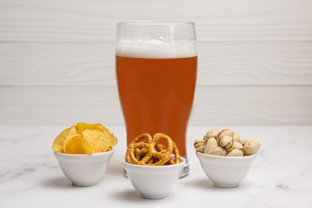 Glass of beer and small bowls with three of the most popular snacks for beer - potato chips, salty mini pretzels and roasted salted pistachios.