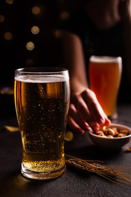 A glass of beer on the table. Woman eating snacks