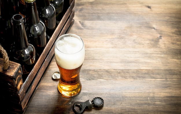 Photo glass of beer with a box and a bottle opener. on a wooden table.