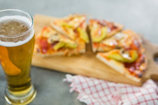 Glass of a beer with pieces of pizza in the background