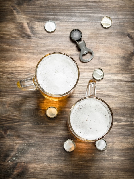 Foto bicchiere di birra con tappi e apribottiglie. su un tavolo di legno.