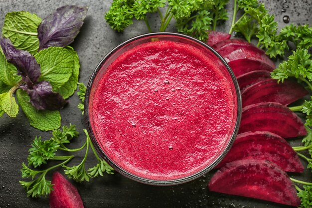 Glass of beetroot smoothie and fresh herbs on table