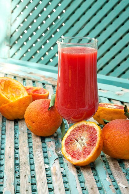 A glass of blood oranges fresh juice on a old green surface. Oranges in the background