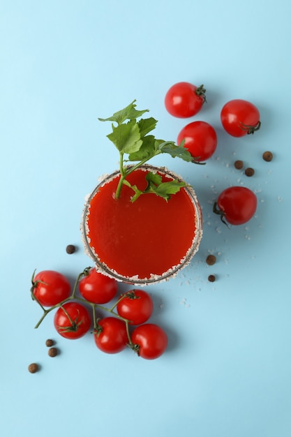 Glass of Bloody Mary and tomatoes on blue background