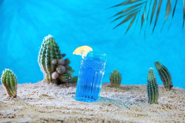 A glass of blue Thai tea on the sand with cacti