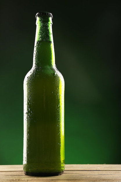 Glass bottle of beer on dark green background