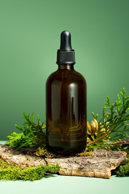 Glass bottle of body oil A conceptual composition of essential oil moss and tree bark on a green background Oil serum for skin and hair care Selfcare and wellness Forest and nature theme