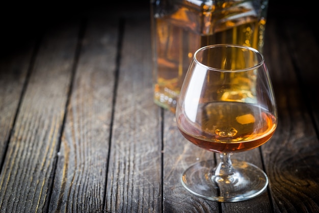 Glass and a bottle of brandy or cognac on the wooden table.