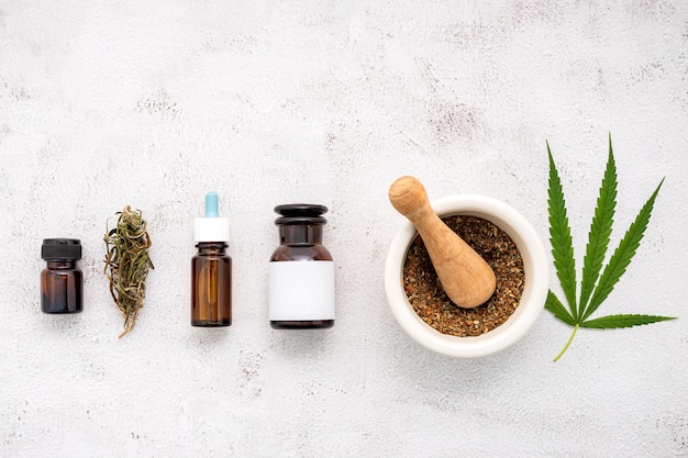 Glass bottle of cannabis oil with white mortar and hemp leaves set up  on concrete.