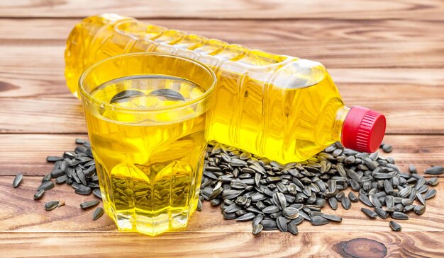 Glass and bottle of cooking oil with heap of sunflower seeds on wooden table