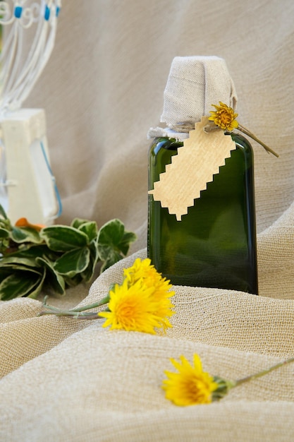 A glass bottle of dandelion oil on a sackcloth. Dandelion blossoms in the background