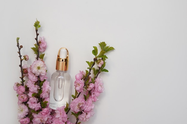 Photo glass bottle of essential oil with fresh pink flowers on white background