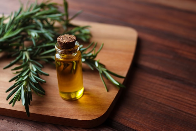 Glass bottle of essential organic rosemary oil with fresh rosemary branches closeup on rustic wooden table