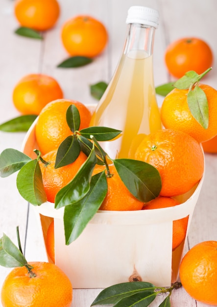 Glass bottle of fresh mandarin tangerine juice in wooden box on light wood background