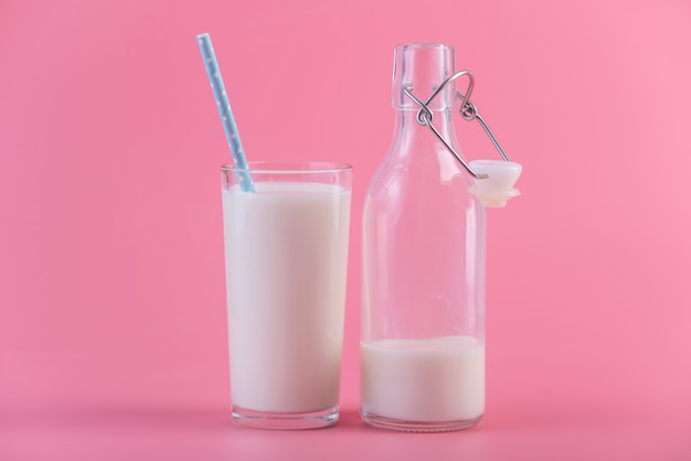 Bottiglia di vetro di latte fresco e un bicchiere con una cannuccia su uno sfondo rosa. latticini sani con calcio