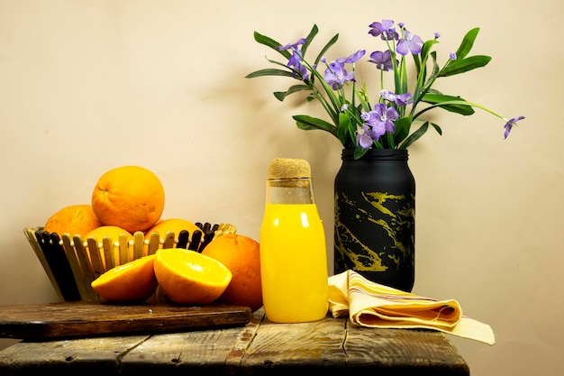 glass bottle of fresh orange juice with fresh fruits and flowers vase on wooden planks table