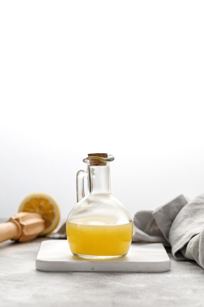 Glass bottle of freshly squeezed lemon juice and ripe lemons on grey background Grey napkin