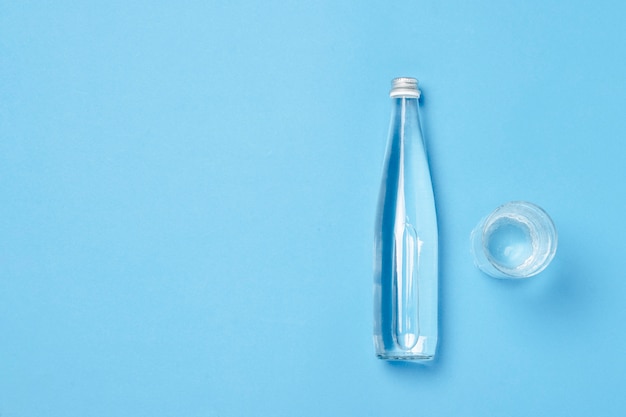 Glass bottle and glass with clear water on a blue space. Concept of health and beauty, water balance, thirst, heat, summer