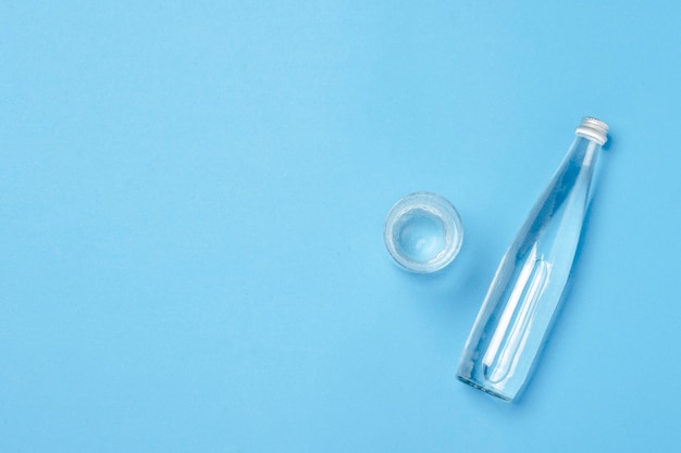 Glass bottle and glass with clear water on a blue surface. Concept of health and beauty, water balance, thirst, heat, summer. Flat lay, top view