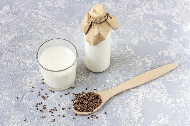 Foto bottiglia di vetro e bicchiere di yogurt con semi di lino, cucchiaio di legno con semi di lino