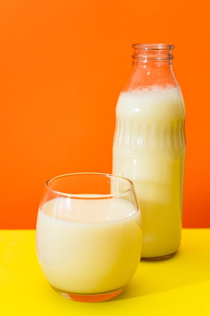 Glass bottle and large glass with milk on a yellow table with orange background Copy space