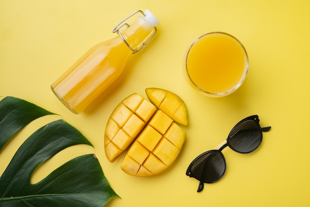 Glass bottle of mango juice set, on yellow textured summer background, top view flat lay