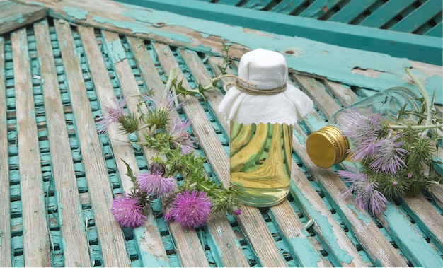 A glass bottle of milk thistle oil. Milk thistle blossoms in the background