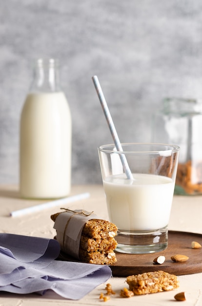 A glass and a bottle of milk with cereal bars some almonds in a jar and a light blue napkin