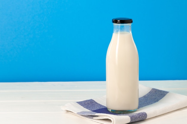 Glass bottle of milk on wooden table against blue background, front view