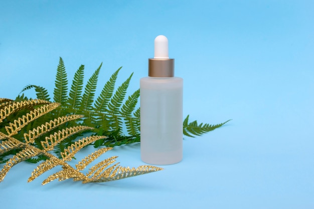 Bottiglia di vetro di olio naturale con foglie di palma di felce d'oro. prodotti cosmetici per la cura della pelle, moderno concetto di tendenza alla bellezza organica.