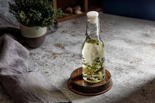 Photo glass bottle of oil with thyme and garlic and pepper on a gray background with a napkin